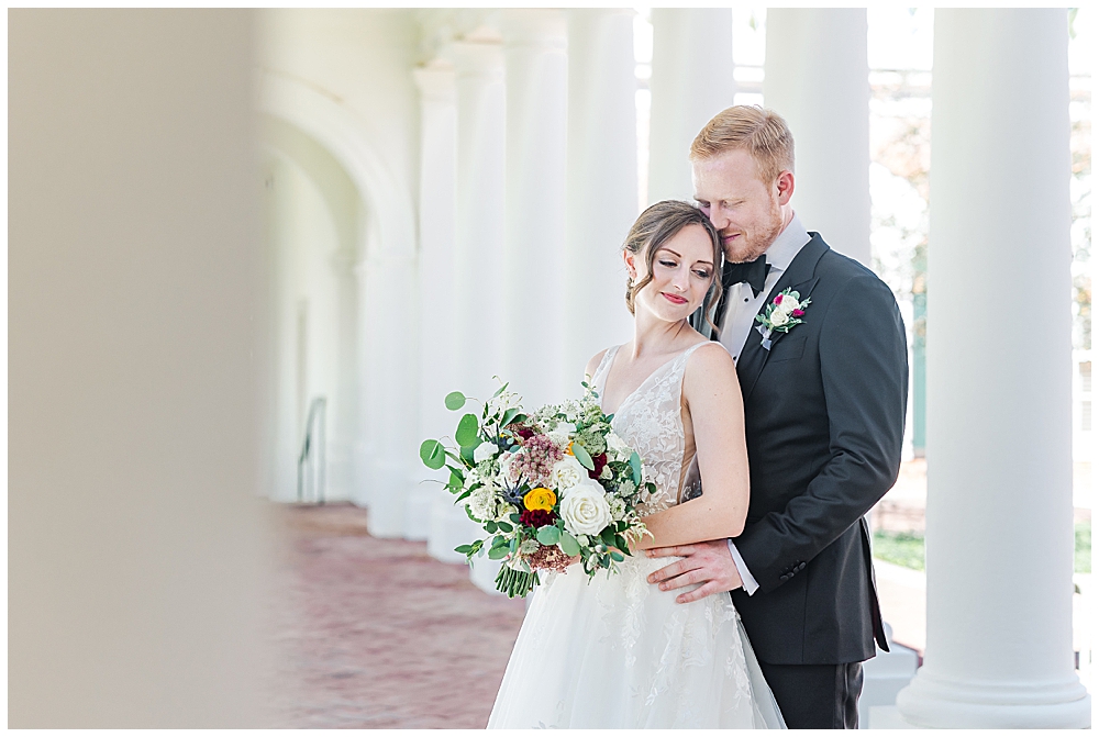 Average Pricing for a Georgia Wedding Photographer | A bride and groom snuggle up against a repeated pillar backdrop, with the bride holding a bouquet of in-season fall florals and eucalyptus greenery