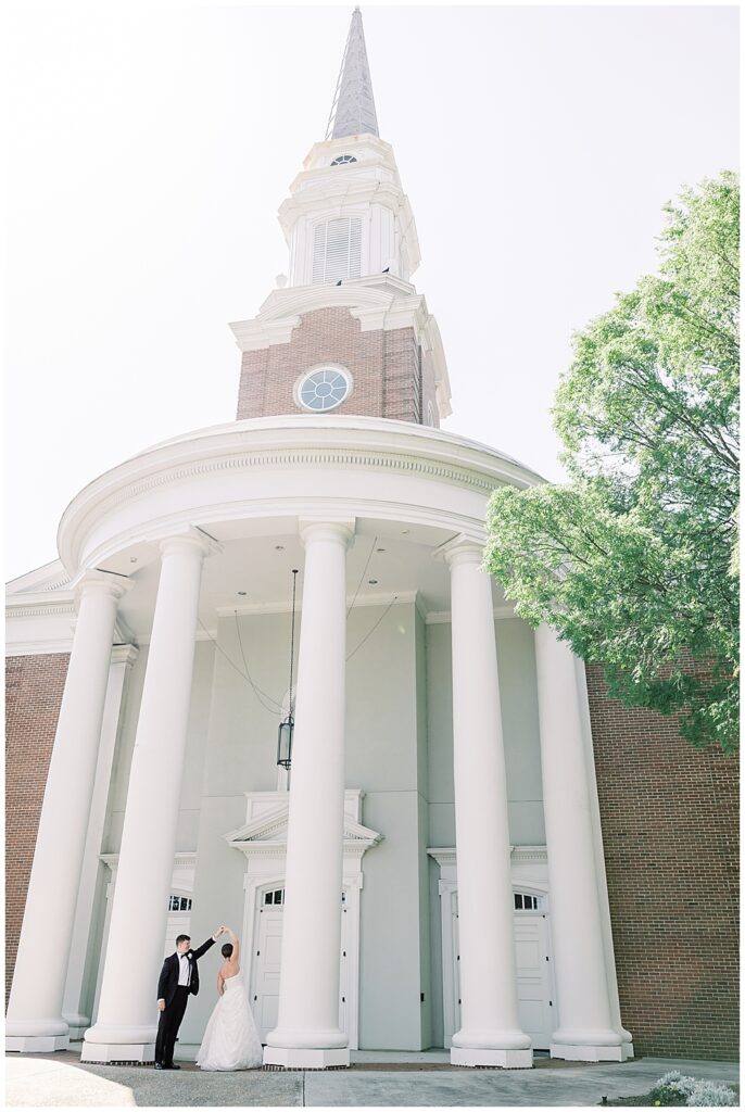 A bride and groom dancing amidst the tall white columns of Dunwoody United Methodist Church before their wedding ceremony