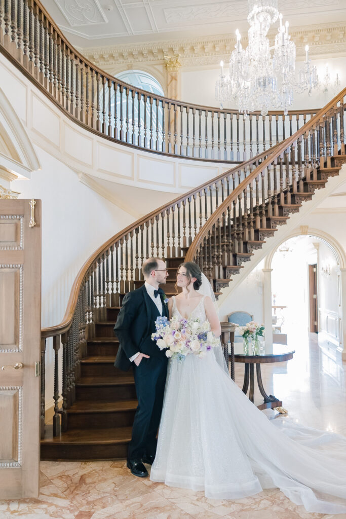 A bride and groom gaze at each other in front of a winding grand staircase in their ornate, historic estate wedding venue on their spring wedding day in Georgia – taken by an Atlanta wedding photographer