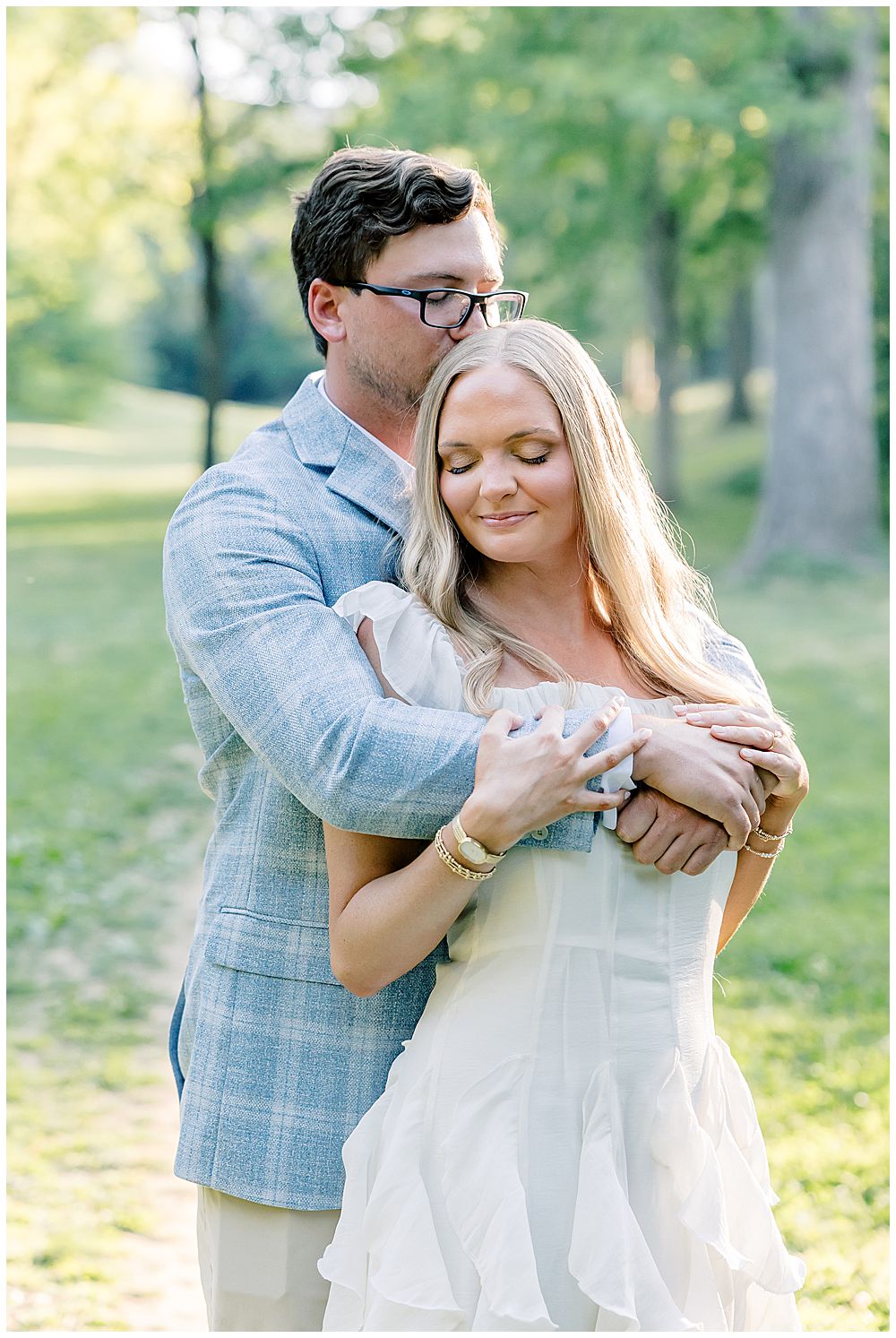An engaged couple embracing at their Winn Park engagement session, the bride wearing a flowy white dress with soft ruffles and the groom wearing a baby blue window-pane pattern blazer | Atlanta wedding photographer